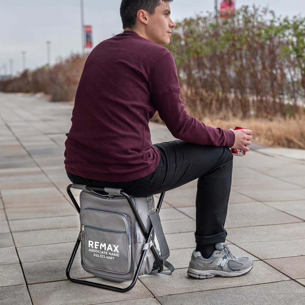 Person sitting on a gray stool with a backpack, outdoors.