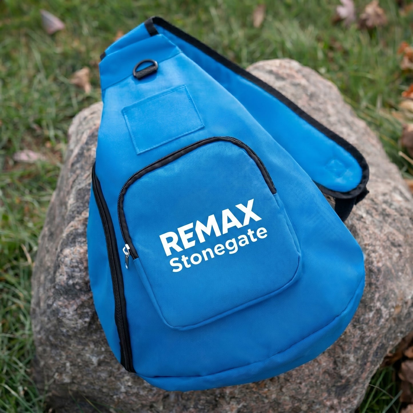 Blue sling bag with 'REMAX Stonegate' logo on a rock outdoors