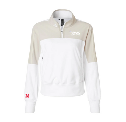 A women's colorblock quarter-zip sweatshirt by adidas, featuring a white body, beige upper chest and sleeves, a white lower sleeve, and a red Nebraska 'N' logo on the left cuff. The right chest features a white 'REMAX CONCEPTS' logo.