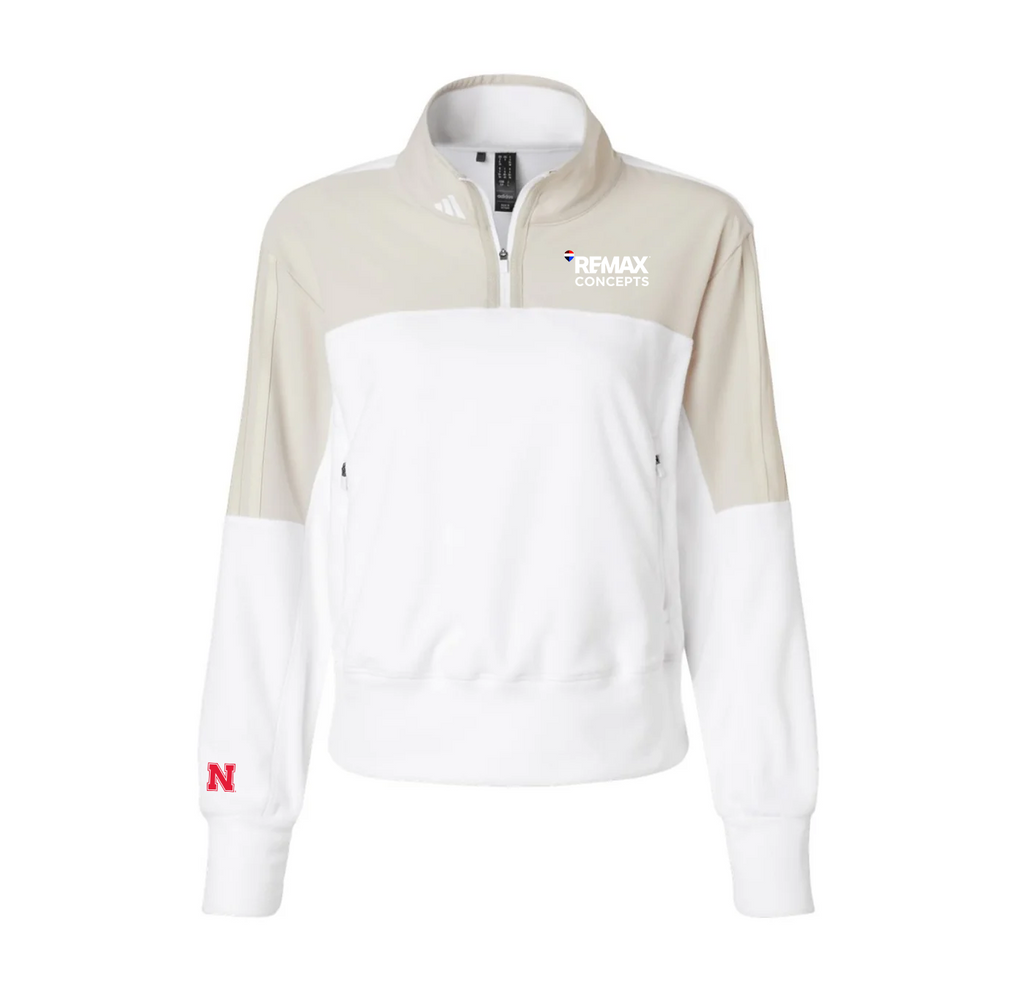 A women's colorblock quarter-zip sweatshirt by adidas, featuring a white body, beige upper chest and sleeves, a white lower sleeve, and a red Nebraska 'N' logo on the left cuff. The right chest features a white 'REMAX CONCEPTS' logo.