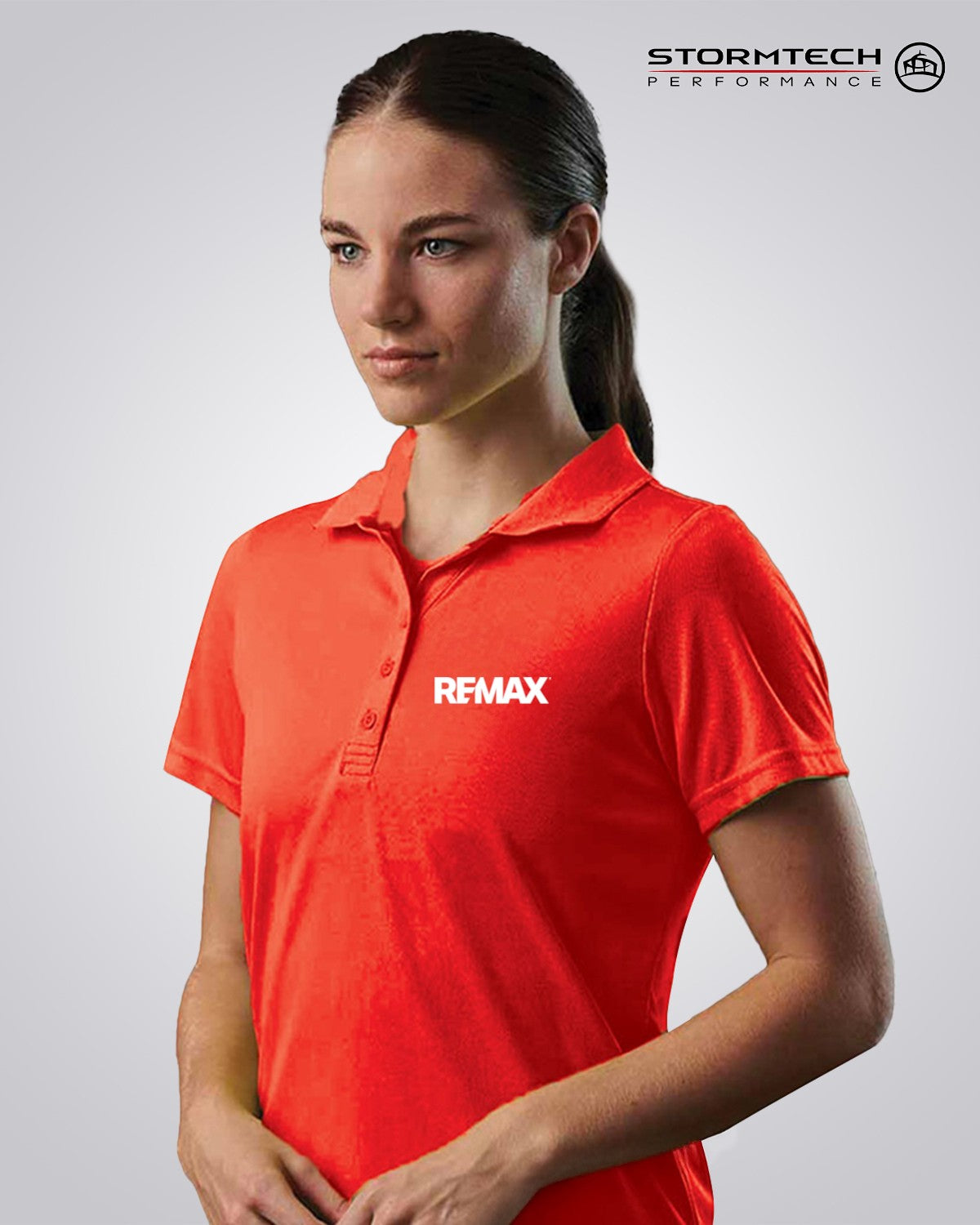 A woman wearing a bright red short-sleeve polo shirt with the white REMAX logo on the left chest, shown against a light gray studio background. The Stormtech Performance logo is visible in the top right corner.