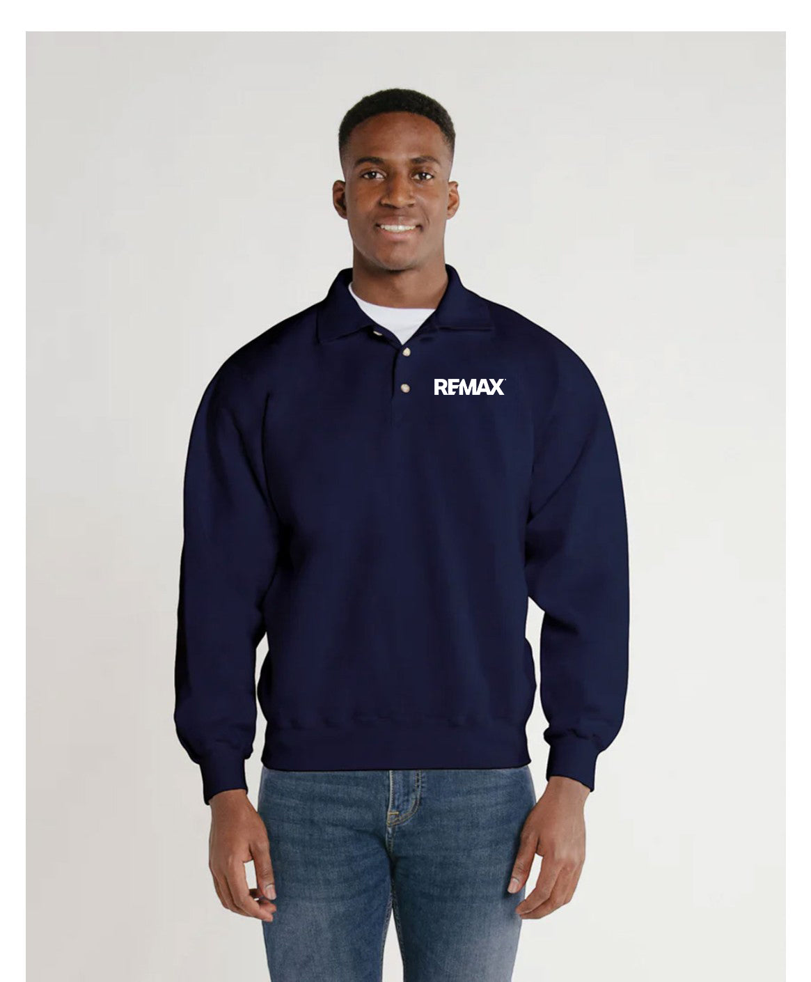A man wearing a navy blue long-sleeve polo-style sweatshirt with a white REMAX logo on the left chest, paired with blue jeans, standing against a light gray studio background.