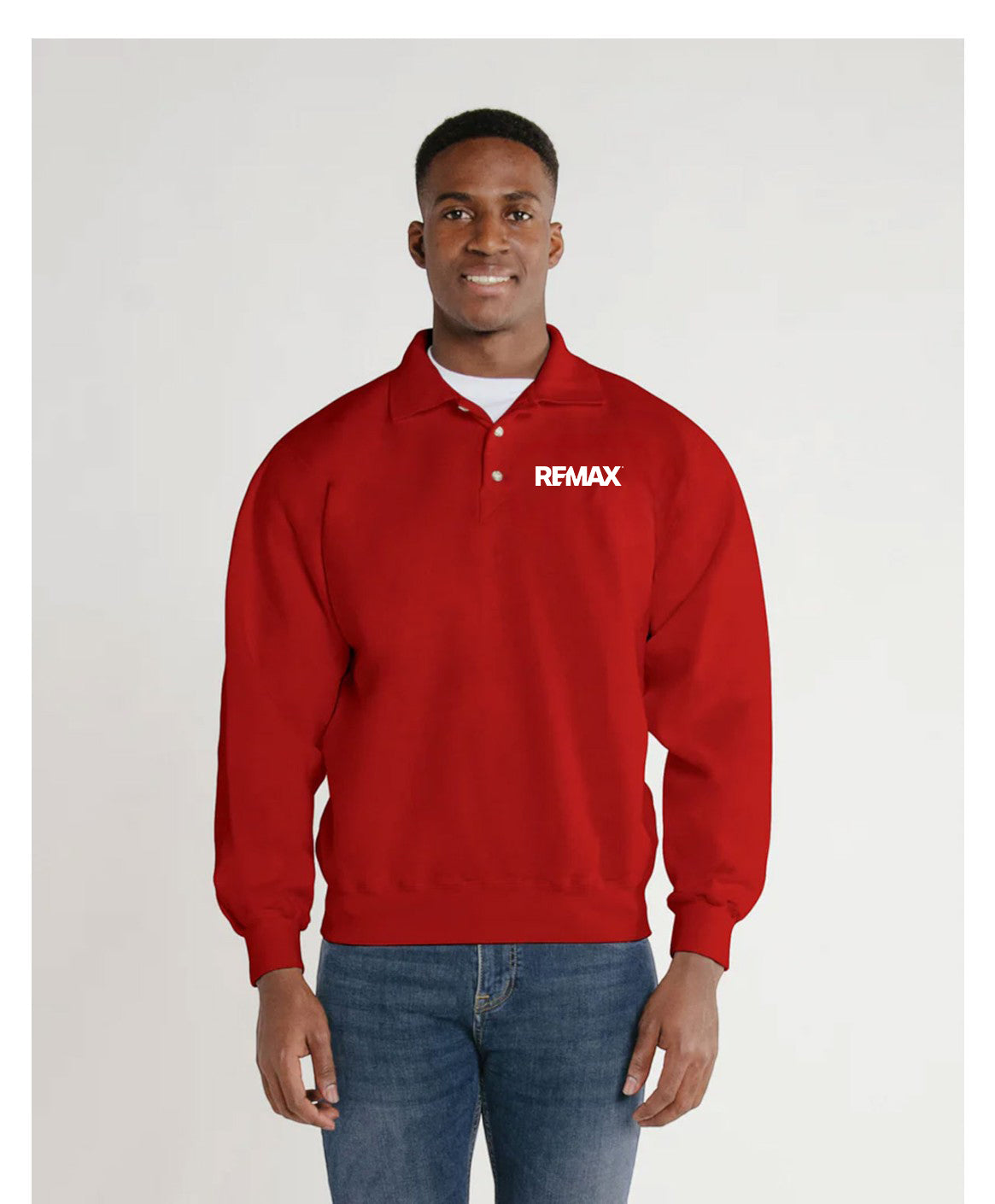 A man wearing a red long-sleeve polo-style sweatshirt with a white REMAX logo on the left chest, paired with blue jeans, standing against a light gray studio background.