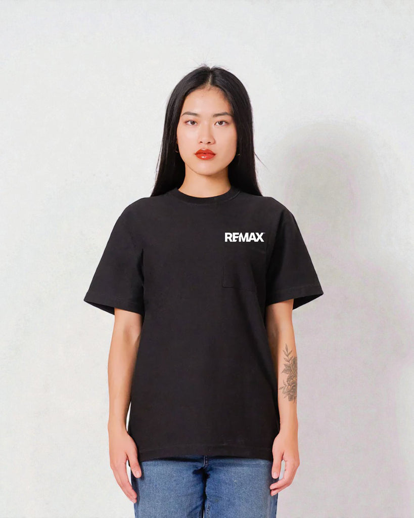 A woman modeling a black short-sleeve t-shirt with the brand name 'REMAX' printed in white on the left chest, paired with blue jeans against a light gray textured wall.