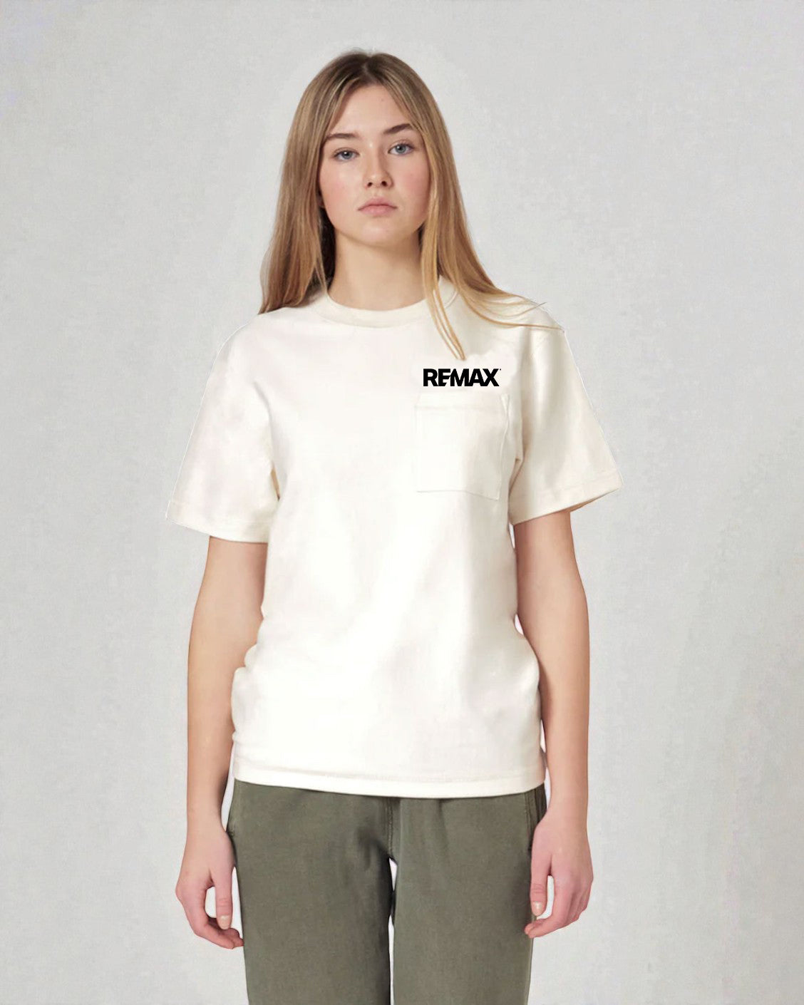 A woman modeling a cream-colored short-sleeve pocket t-shirt with a black 'REMAX' logo on the chest, paired with olive green pants, against a light gray textured studio background.