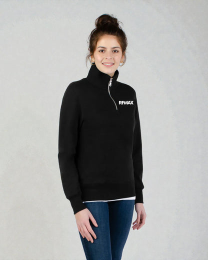 A woman wearing a black quarter-zip mock neck sweater with a white 'RFMAX' logo on the chest, paired with blue jeans, standing against a light gray textured background.
