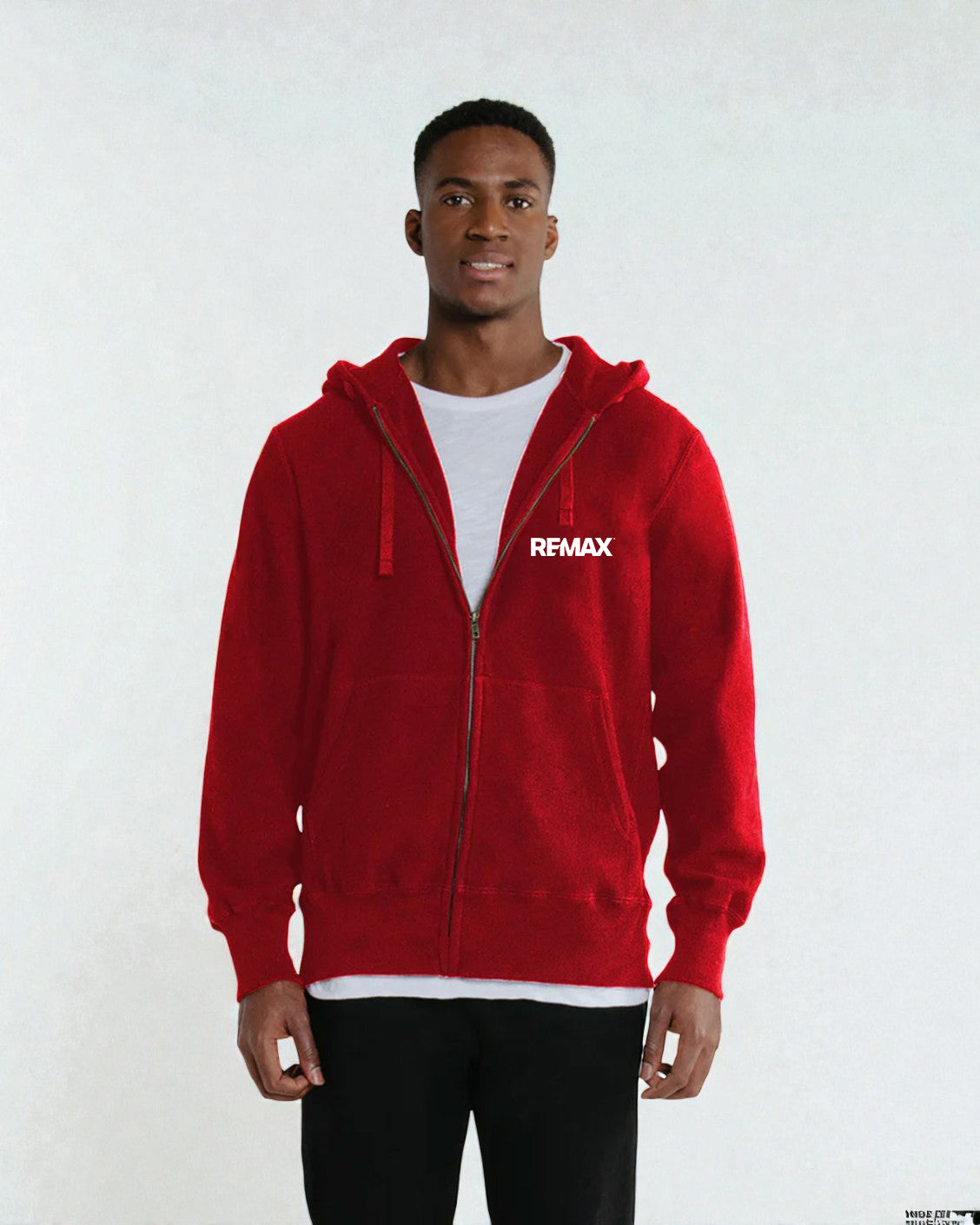 A man wearing a red zip-up hoodie with a white REMAX logo on the chest, layered over a white t-shirt and black pants, standing against a light gray background.