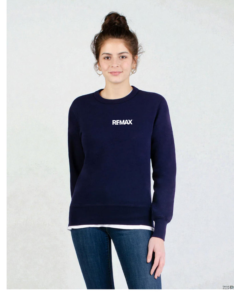 A woman wearing a navy blue crewneck sweatshirt with the word 'REMAX' printed in white on the chest, paired with dark blue jeans, standing against a light gray textured wall.