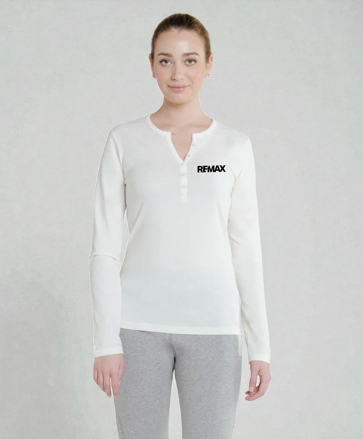 A woman modeling a white long-sleeve henley shirt with a small black REMAX logo on the left chest, paired with gray sweatpants, against a light gray textured studio background.
