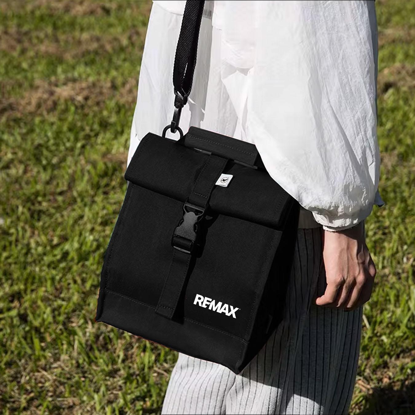 Person holding a black REMAX bag outdoors on grass