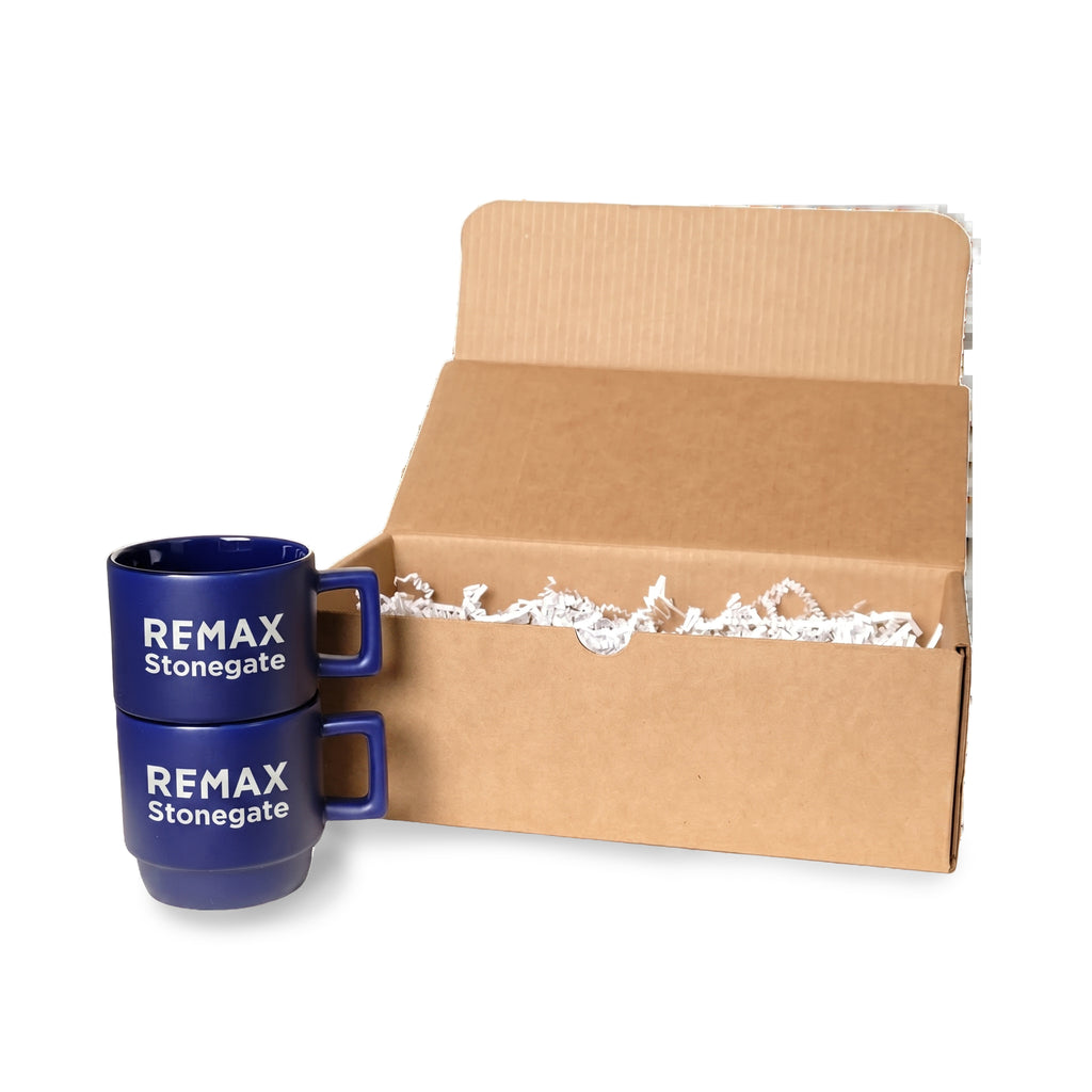 Two blue mugs with 'REMAX Stonegate' branding in front of an open cardboard box.