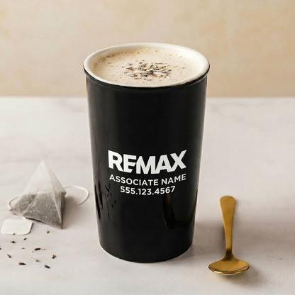 Black mug with REMAX branding on a light surface with a tea bag and spoon.