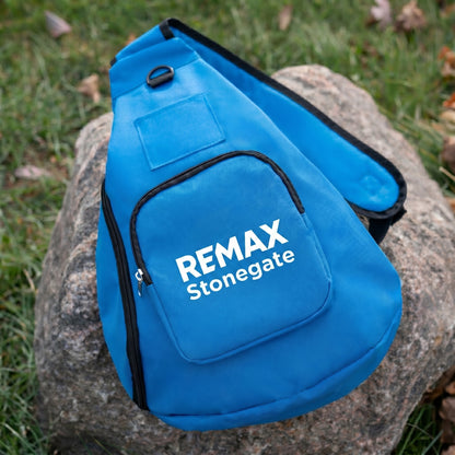Blue sling bag with 'REMAX Stonegate' logo on a rock outdoors