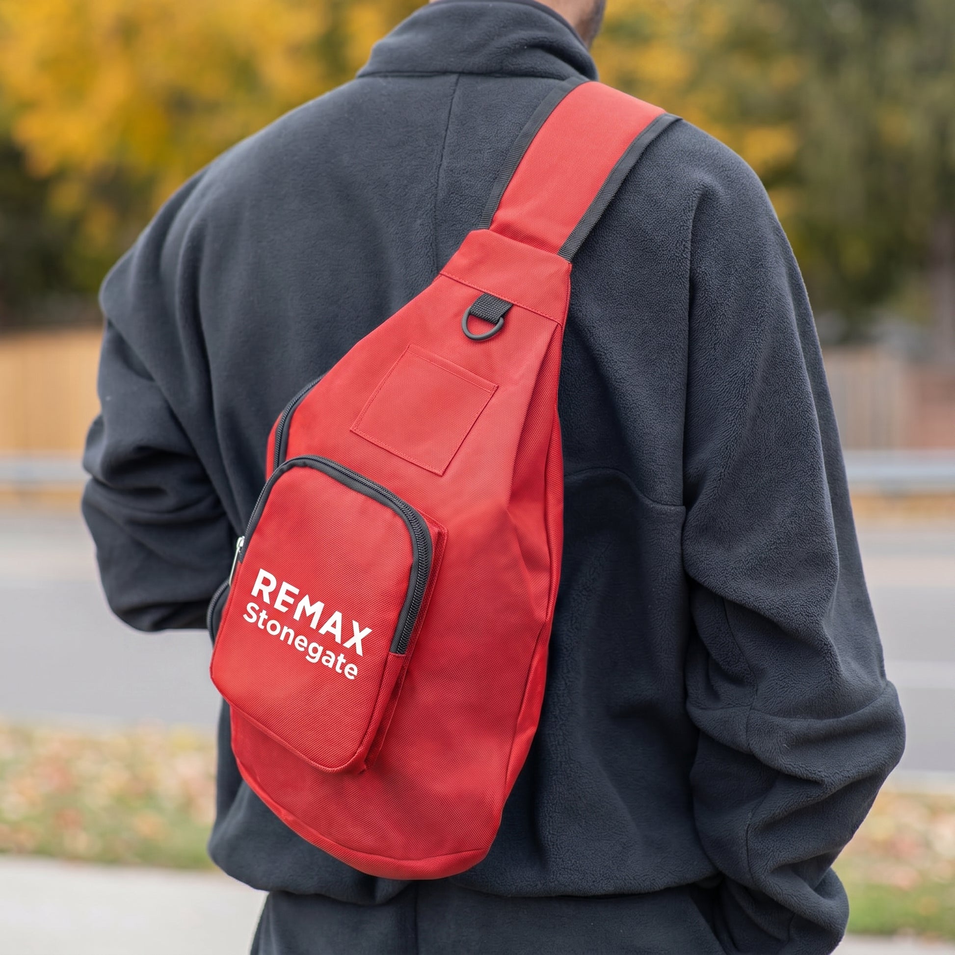 Person wearing a red sling bag with 'REMAX Stonegate' logo outdoors.
