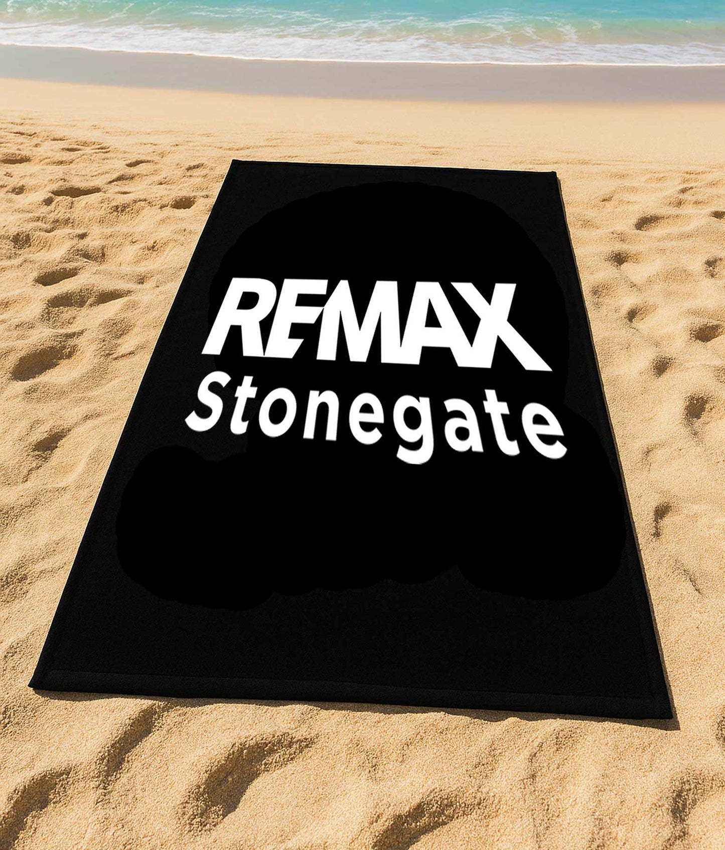 Black mat with 'REMAX Stonegate' text on a sandy beach