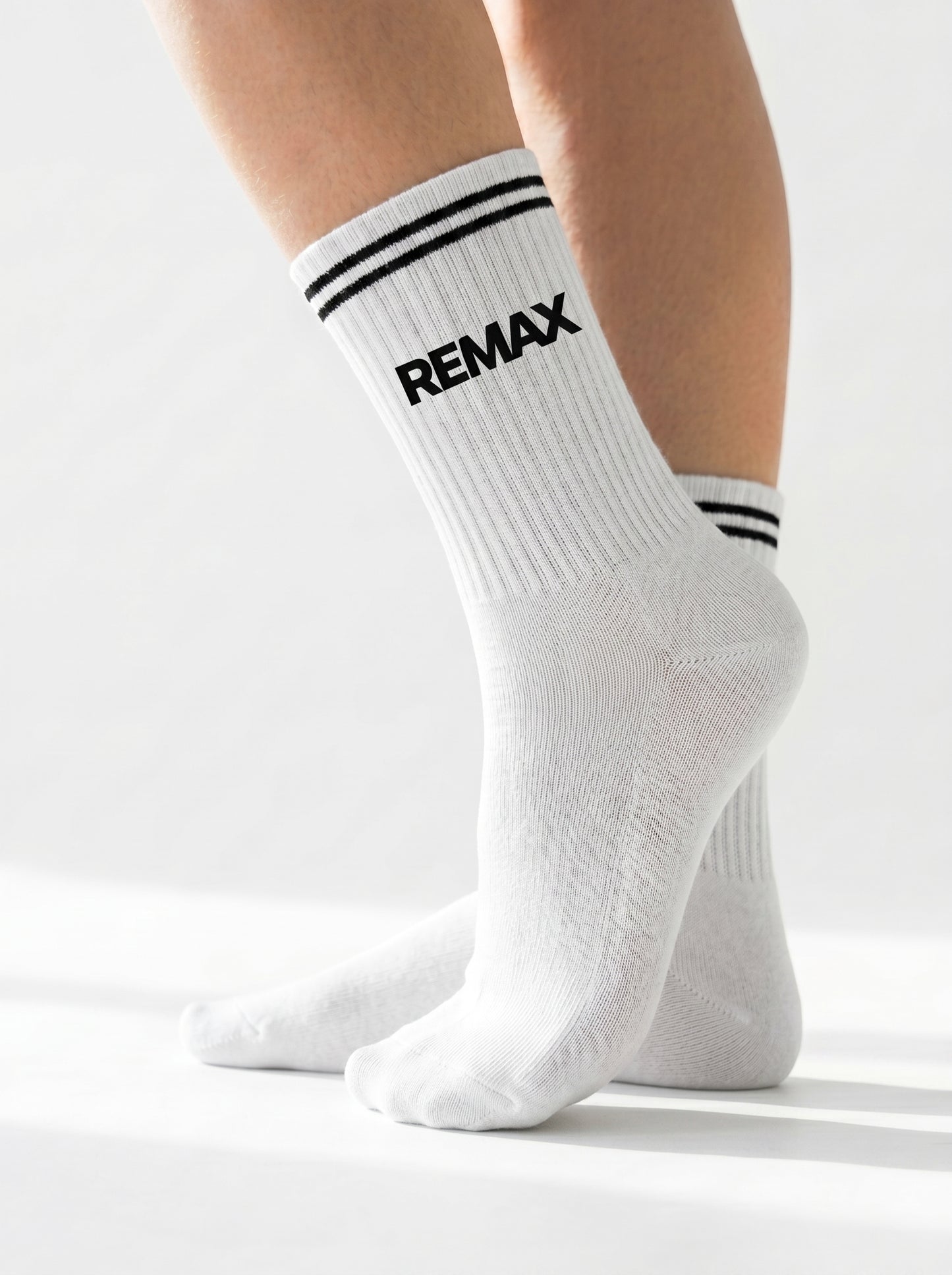 White socks with black stripes and 'REMAX' logo worn by a person on a white background