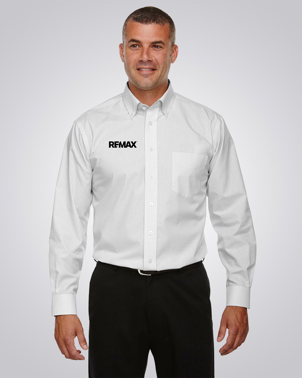 A man wearing a white long-sleeve button-down shirt with a black REMAX logo on the left chest, paired with black trousers, against a light gray studio background.