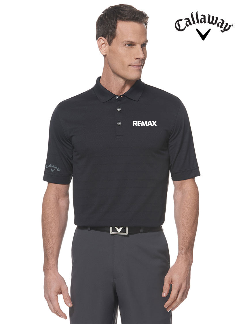 A man modeling a black Callaway Remax short-sleeve polo shirt with a white logo on the chest, paired with dark gray trousers, against a plain white background.