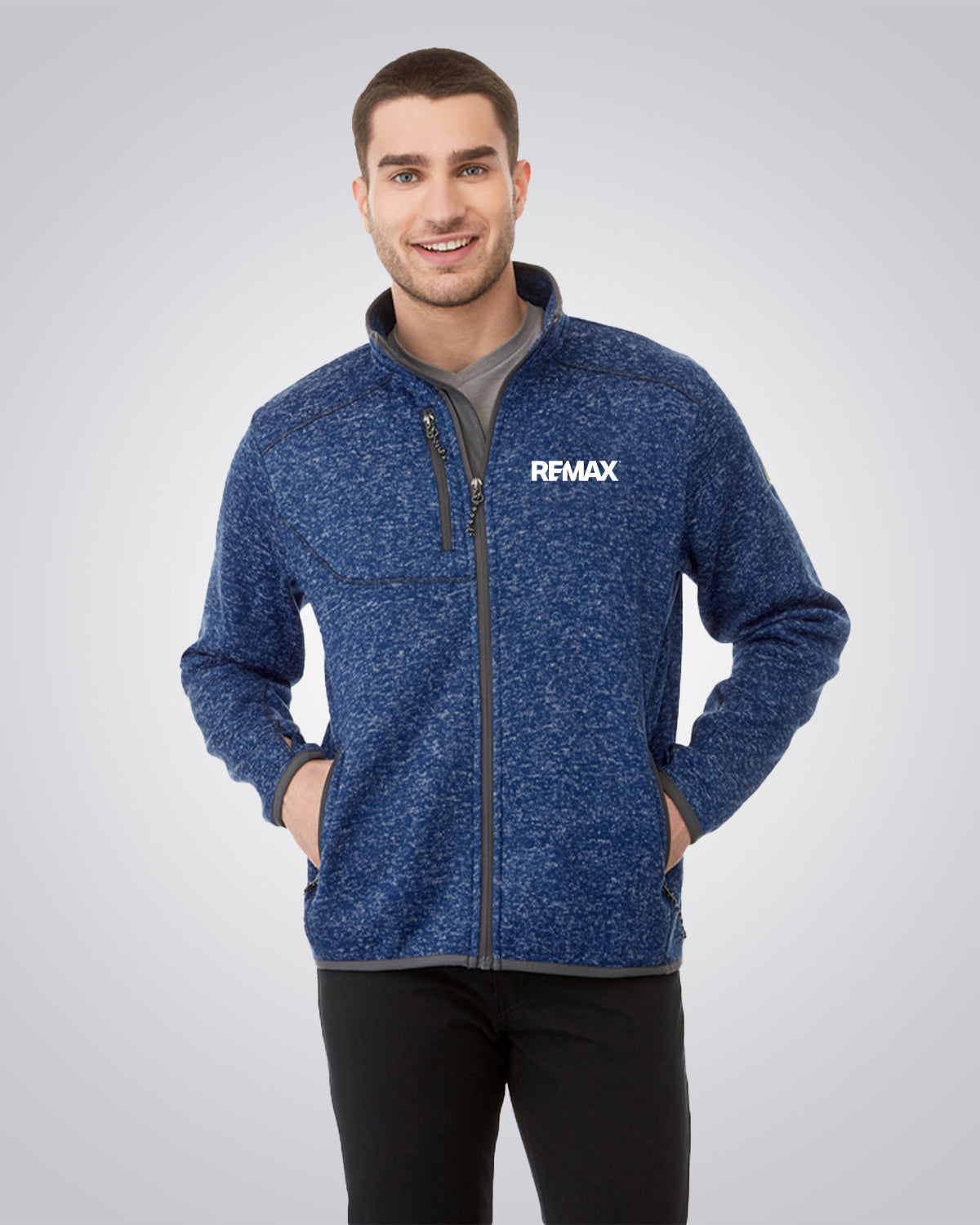 A man wearing a blue heathered zip-up fleece jacket with a gray inner collar and the brand name 'REMAX' printed in white on the left chest, paired with black pants, against a light gray studio background.