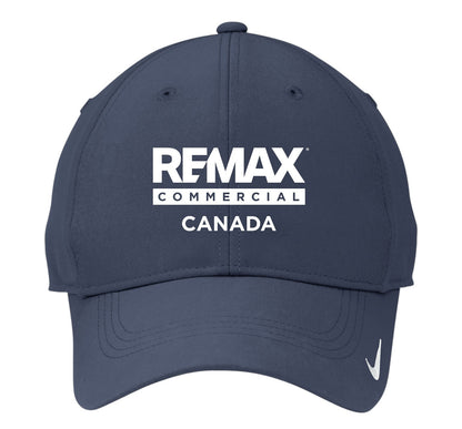 A navy blue baseball cap featuring a white embroidered 'REMAX COMMERCIAL CANADA' logo on the front and a small white Nike swoosh on the side, set against a plain white background.