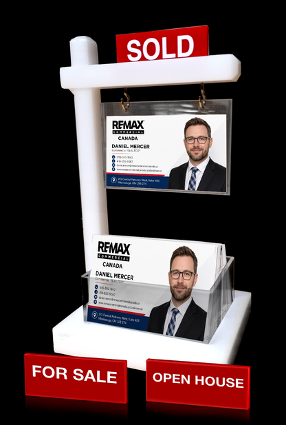 A white real estate sign holder display stand with red 'SOLD' and 'FOR SALE' signs, holding two printed business cards featuring a man's portrait and 'REMAX REALTY CANADA' branding, set against a black background.