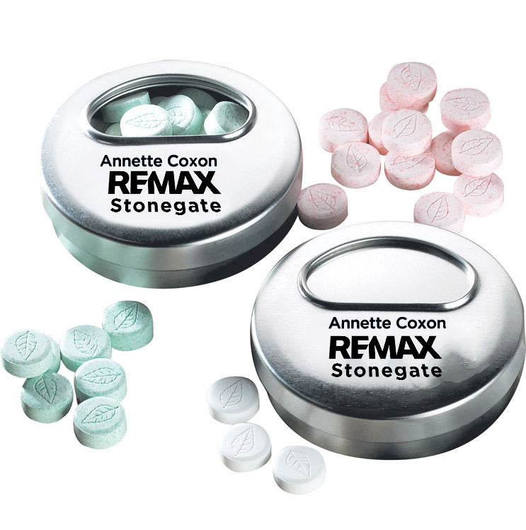 Two metal containers with 'Annette Coxon REMAX Stonegate' branding, one filled with pink pills and the other with green pills.